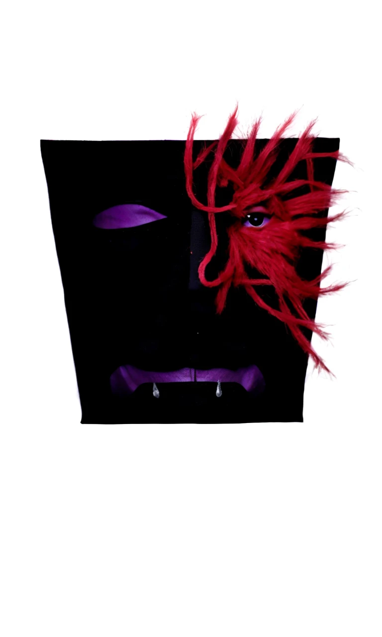 A man in a black mask with a black eye and a purple mouth sewn on, with one side of the mask cracked with red