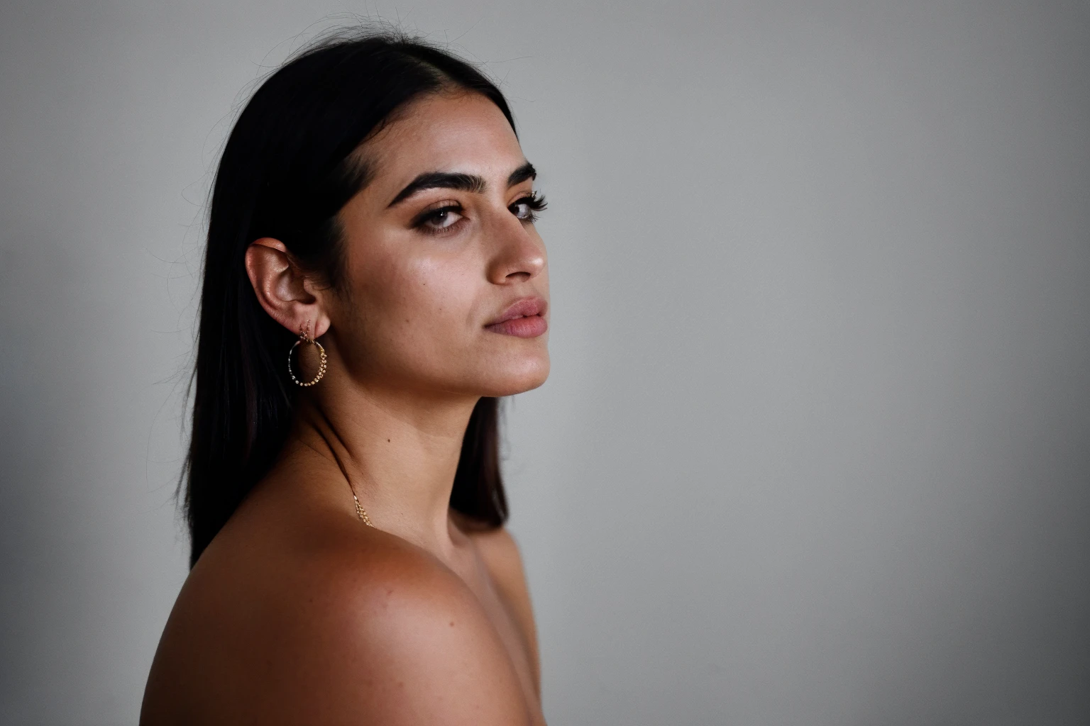 RAW photo,dark,moody,hazy atmosphere,35mm focal lenght,underexposed,cold,candid photograph,artistic,full body,photo of a beautiful,influencer,30yo Iranian woman,detailed skin,naked, looking away from viewer, thick body structure,grey background,no background, candid pose,dim room,blue light, film grain, kodak color, instagram LUT
