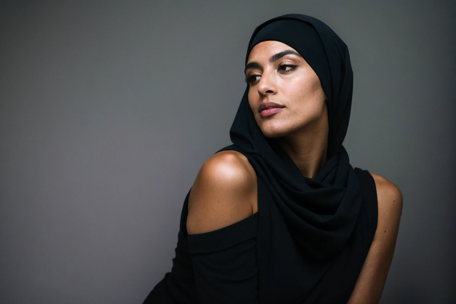 RAW photo,dark,moody,hazy atmosphere,35mm focal lenght,underexposed,cold,candid photograph,artistic,full body,photo of a beautiful,influencer,30yo Moroccan woman,black hijab,detailed skin,naked, looking away from viewer, thick body structure,grey background,no background, candid pose,dim room,blue light, film grain, kodak color, instagram LUT