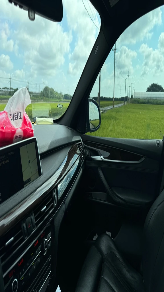 Sit in the passenger seat facing the driver,Photographed from the driver, perspective,2014 BMW X5M interior,The ceiling and leather parts inside the car are all black.,32Hcup,Off-the-shoulder red dress,Low-cut V-neck short skirt red dress,Eyes on the driver,Ma Guang Elementary School as the background,Showing breasts,Use the photos I uploaded to capture the angle and interior of the car.