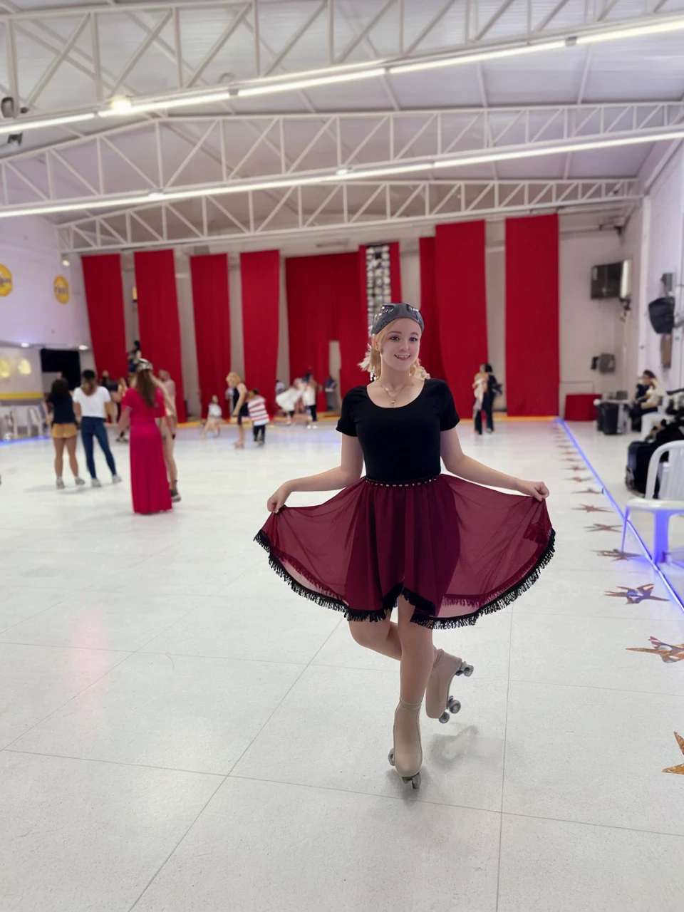 with blond hair reaching the shoulder and fair skin, dancing on white skates, smooth and clear background she wears a red skirt and a black bodysuit She is a ager roller quad skates