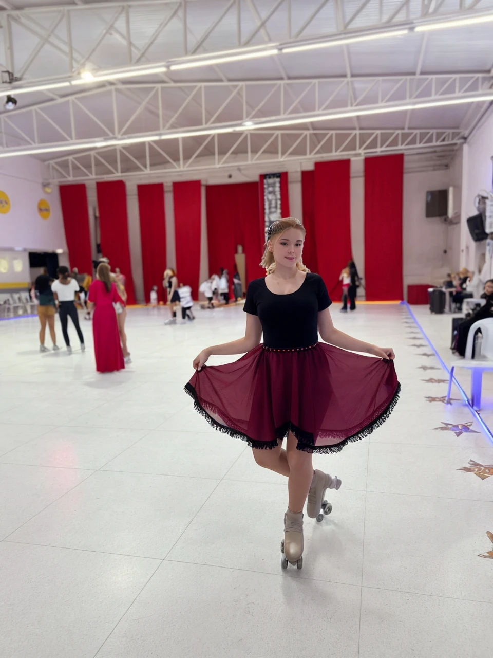 with blond hair reaching the shoulder and fair skin, dancing on white skates, smooth and clear background she wears a red skirt and a black bodysuit She is a teenager roller quad skates