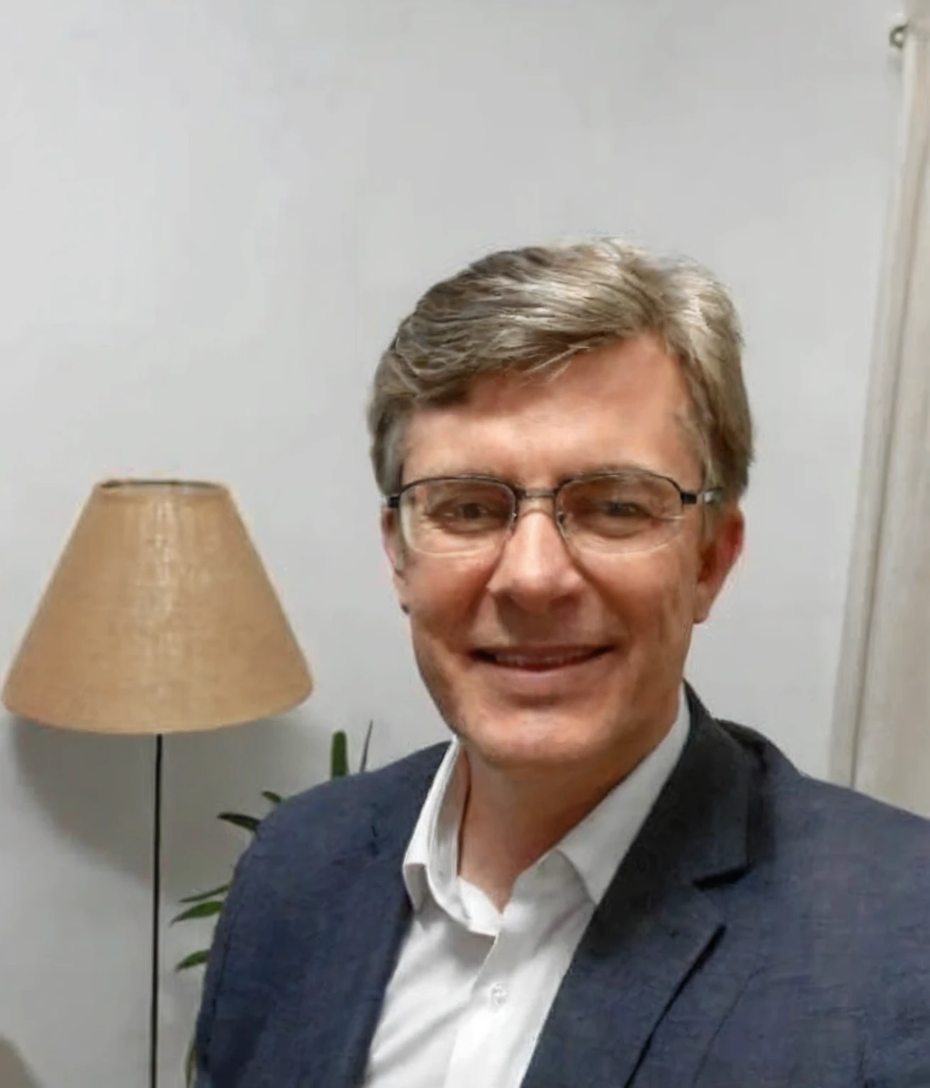 smiling man in a blue suit and glasses in front of a lamp, with a 50 year old face