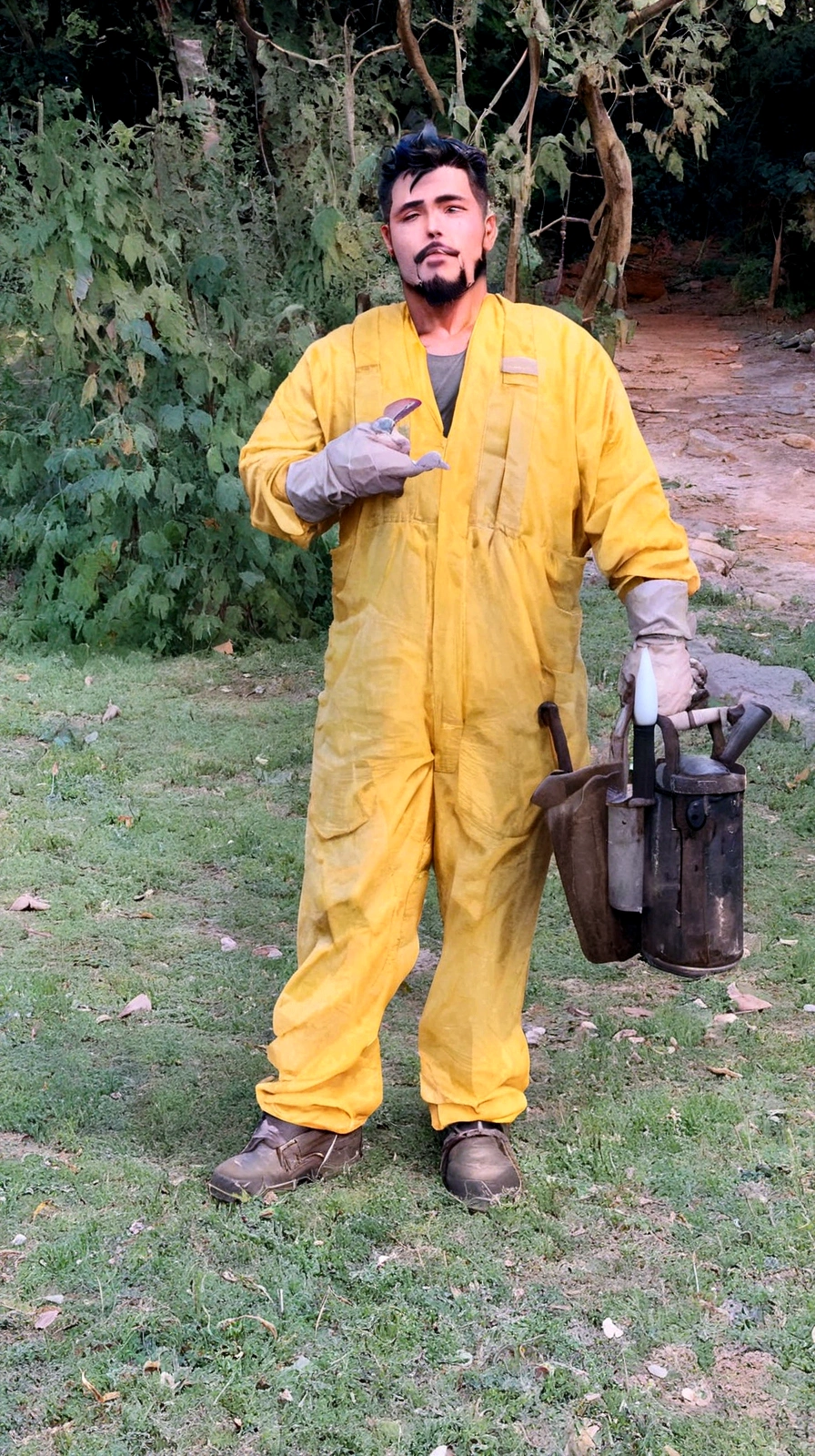 man with light skin, black hair and goatee, in yellow beekeeper overalls holding a fumigator in his right hand