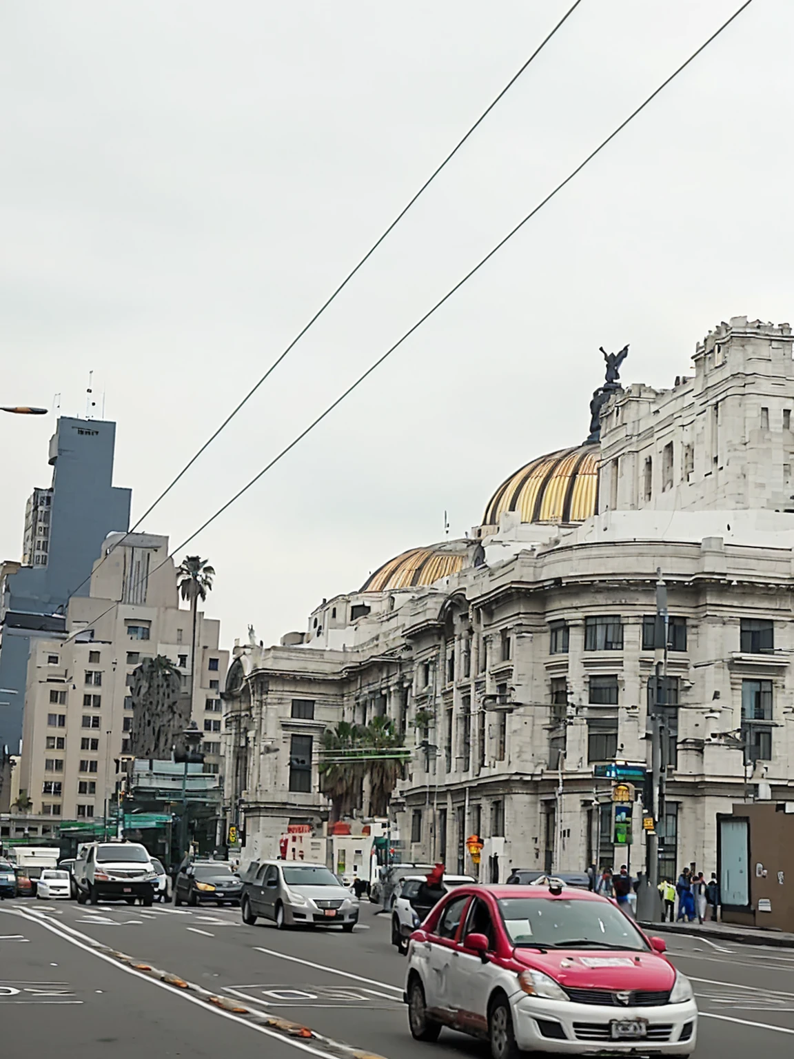 Cars drive on a city street with a building in the background., center mexico, Mexico City, surrounding the city, View from across the street, Lots of construction, edificios épicos en el center, in a city with a rich history, View from the streets, center, Lots of constructions, Big buildings, Building in the distance, white marble buildings, seen from outside, HD, 4k, Good Quality
