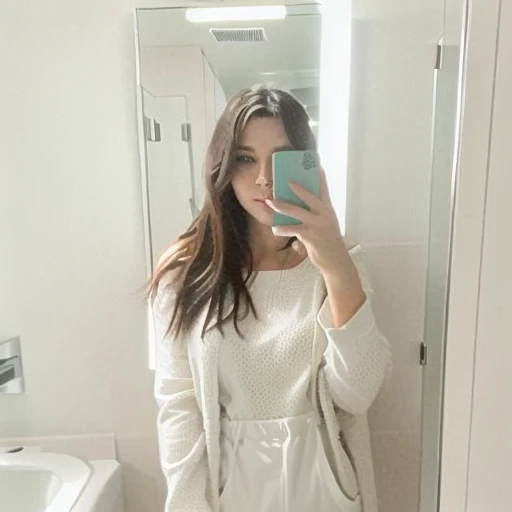 woman taking a selfie in a bathroom mirror, facing camera