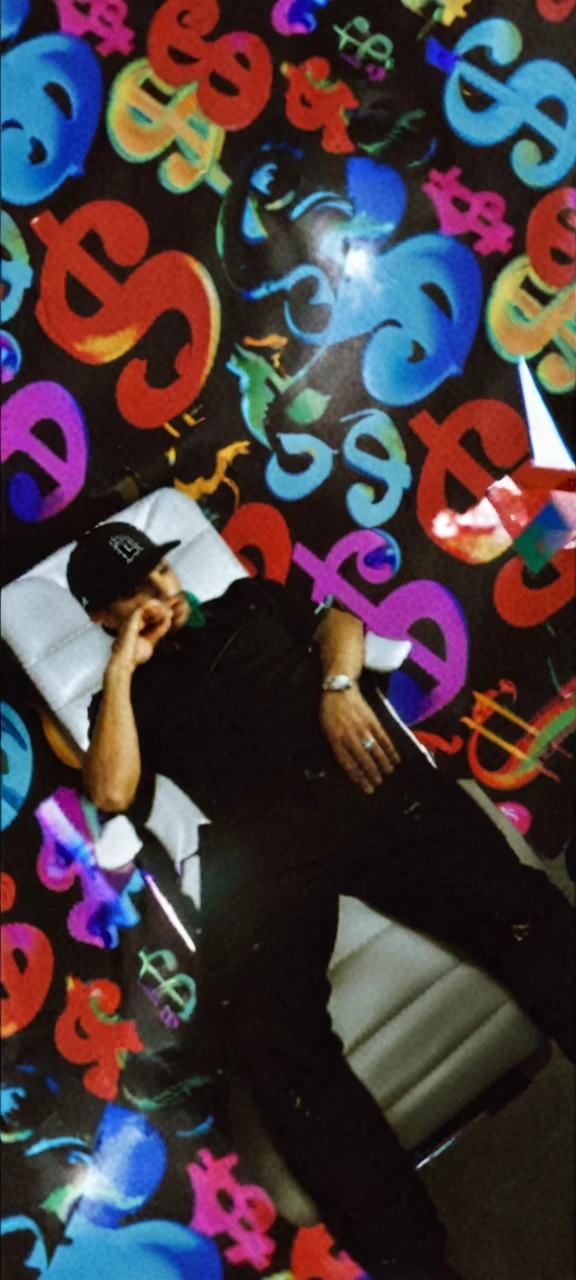 A handsome man wears a black cap with the monopoly logo, He wears black clothing and is sitting with a confident pose on a white leather executive chair with chrome details.
