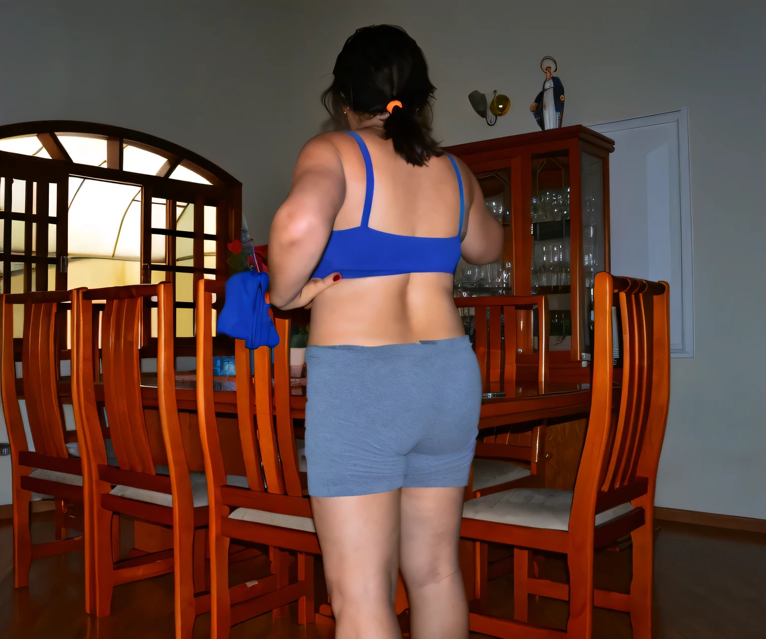 there is a woman standing in a room with a table and chairs, back - shot, back shot, shot from the back, side shot, rear-shot, view from the back, sport bra and dark blue shorts, backview, rear shot, from back, from the back, seen from the back, backshot, photo from the back, back - view