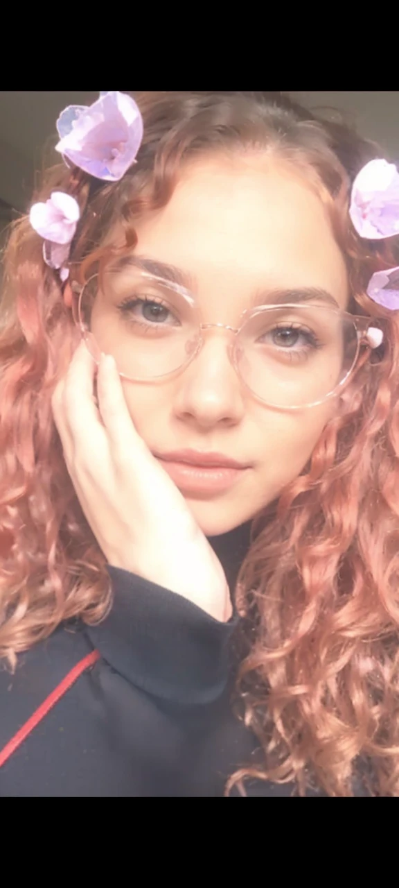 a young woman with small breasts wearing a low-cut red crop top, without bra. She has light brown skin with a young face and curly red hair.. Wear transparent glasses, your hair is loose. she is in a sexy position and her body is not thin