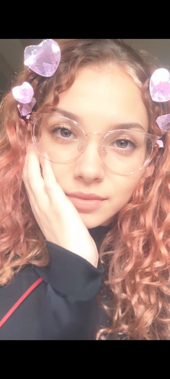 a young woman with small breasts wearing a low-cut red crop top, without bra. She has light brown skin with a young face and curly red hair.. Wear transparent glasses, your hair is loose. she is in a sexy position and her body is not thin