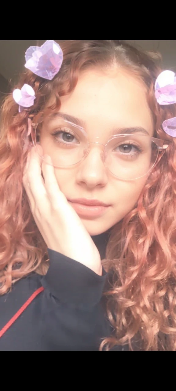 a young woman with small breasts wearing a low-cut red crop top, without bra. She has light brown skin with a young face and curly red hair.. Wear transparent glasses, your hair is loose. she is in a sexy position and her body is not thin