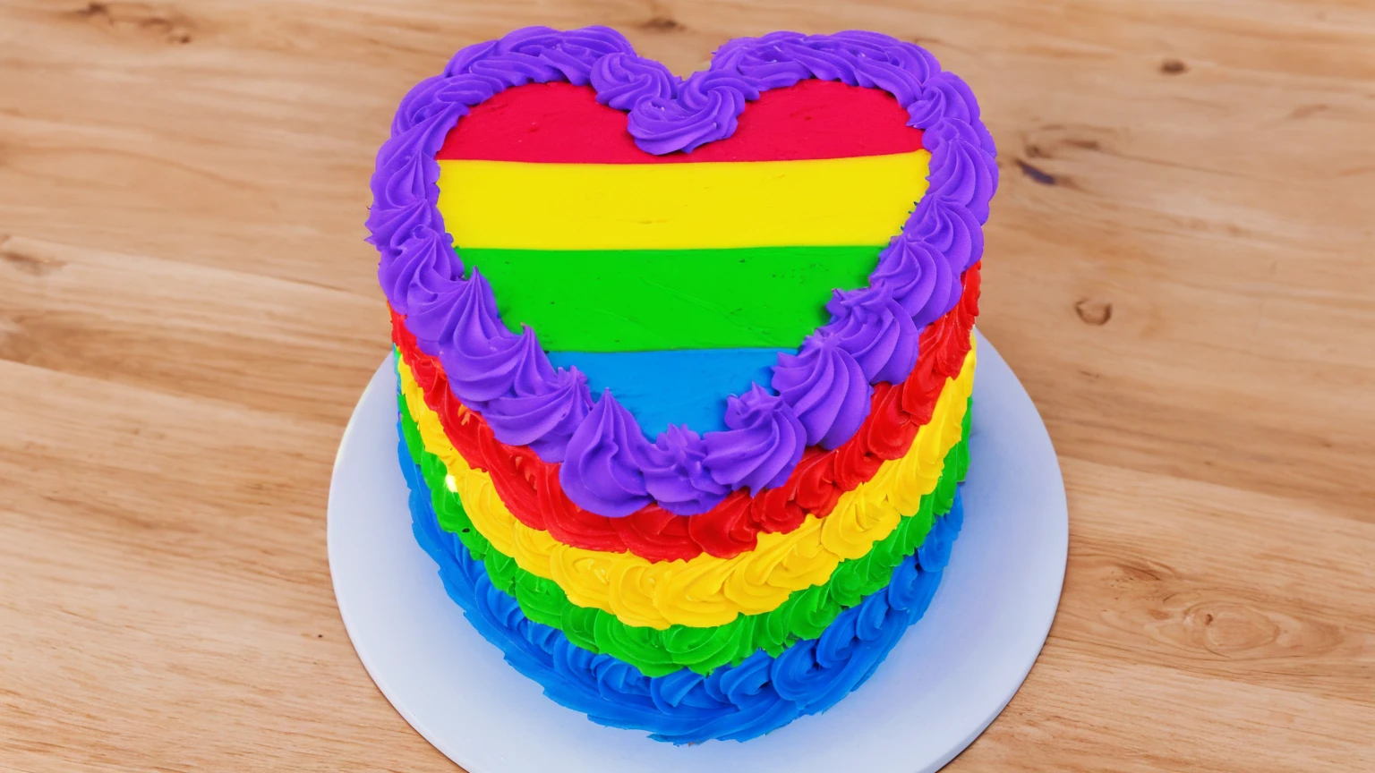 on a wooden table, there is a white plate with a heart cake , rainbow cream heart cake ( star shaped) , multi-colored heart on top, decorated with purple cream, cream with highlights, view from above,  Beautiful light from the window, beautiful lighting, bright announcement, Multiple light sources, Realistic style, realistic textures, high quality, high detail, detailed textures, ultra 4k hd, macro photography