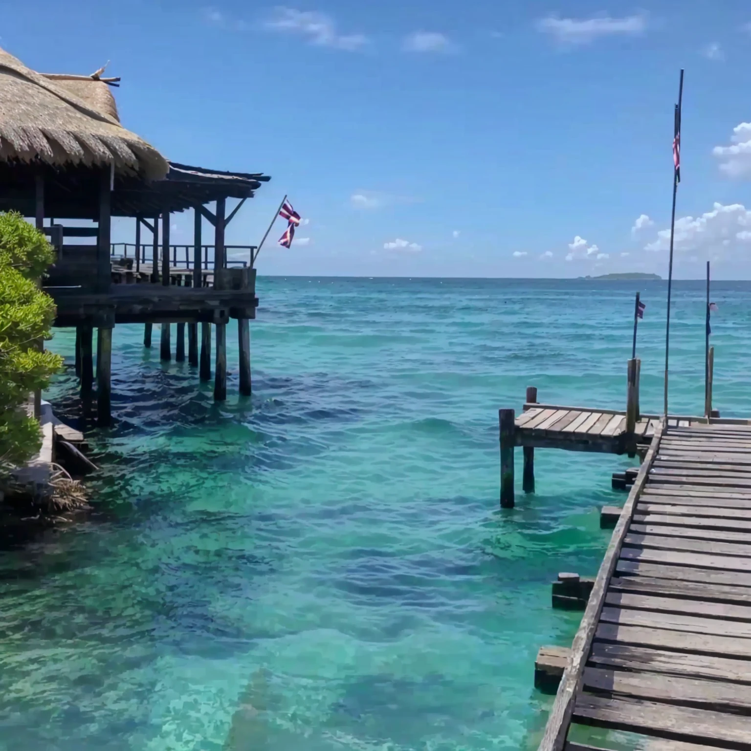 A pier with a thatched roof，There&#39;s a flag hanging on it, crystal clear blue water, carribean turquoise water, crystal Shimizu, turquoise water, clear blue water, wonderful masterpiece, On the water, sapphire waters below, Blue water, Shimizu, Clear water, azure water, Stunning sight, Tropical Regions, Paradise in the background