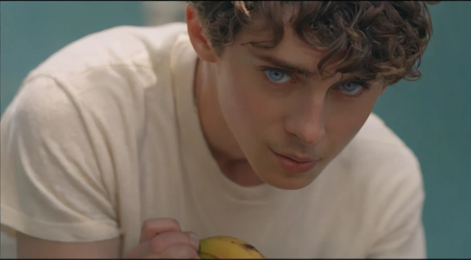 There was a young man holding a banana in his hand, Pretty Boy, Timothy Chalamet, his frank blue eyes, YouTube 视频screenshot, 音乐视频screenshot, a24 Cinematography, Declan McKenna, screenshot, High-quality movie stills, a24!Cinematography, he has short curly brown hair, screenshot, tyler