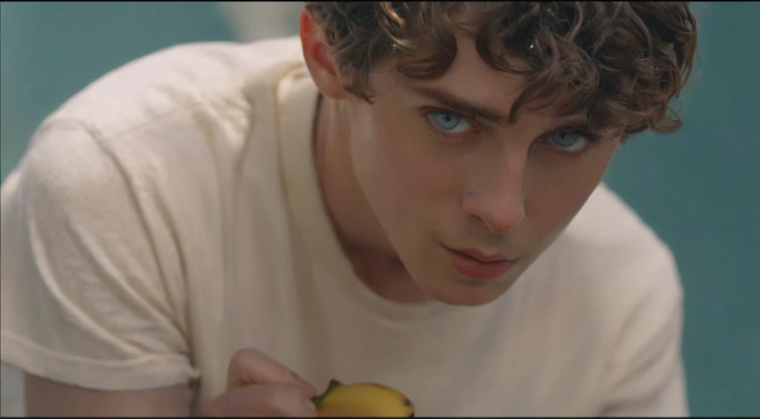 There was a young man holding a banana in his hand, Pretty Boy, Timothy Chalamet, his frank blue eyes, YouTube 视频screenshot, 音乐视频screenshot, a24 Cinematography, Declan McKenna, screenshot, High-quality movie stills, a24!Cinematography, he has short curly brown hair, screenshot, tyler