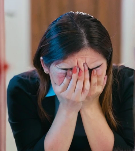 People holding a knife behind a person in front with their hands on their face crying 