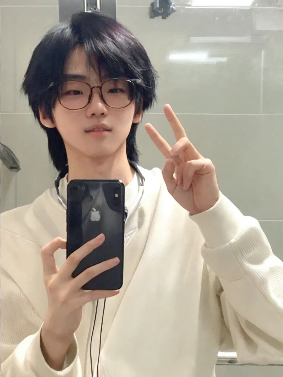 Asian boy. Features: looking at the camera + Holding the cell phone with one hand and the other hand raised, with both fingers raised + thin face + delicate skin + Wear glasses