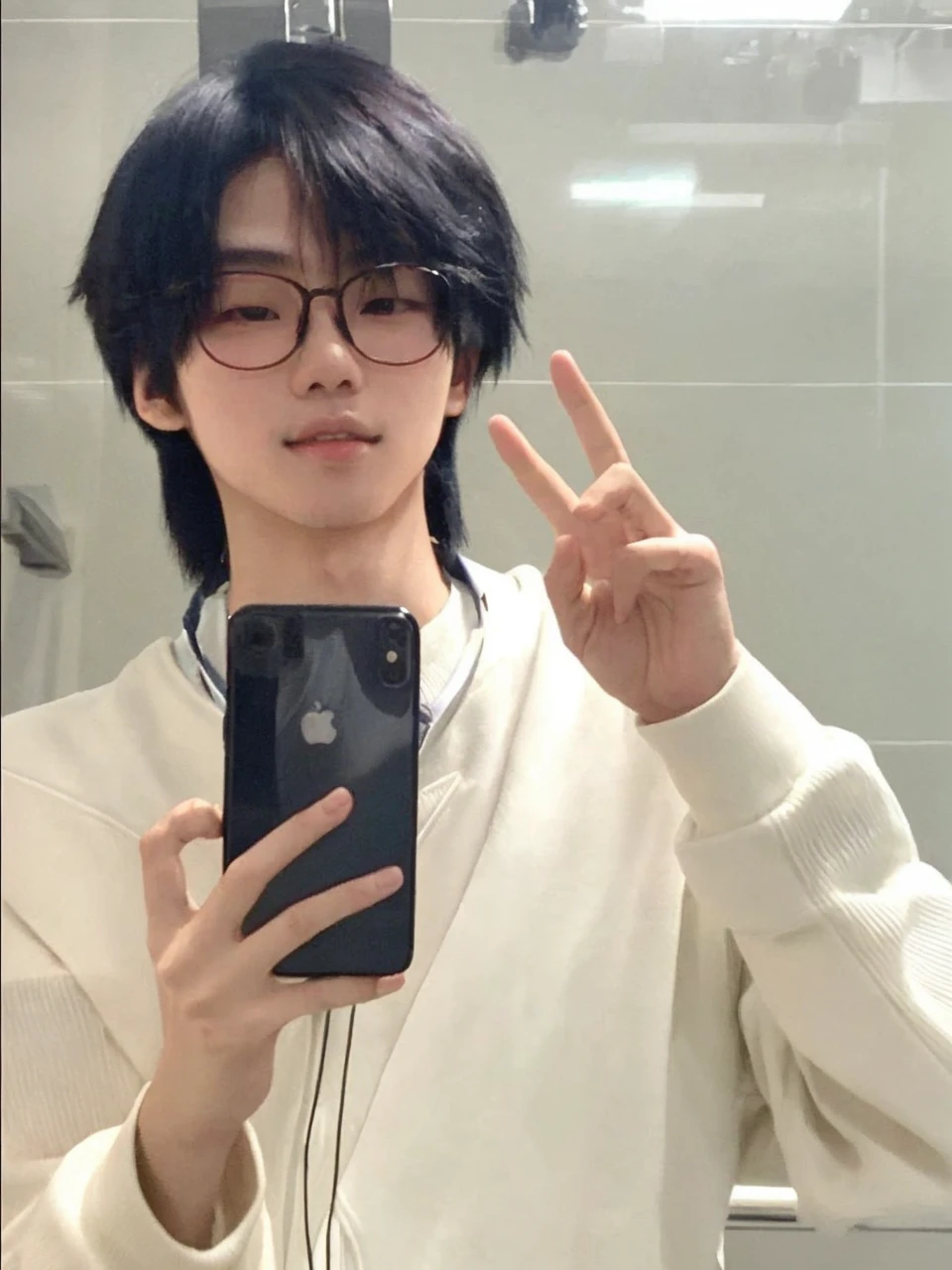 Asian boy. Features: looking at the camera + Holding the cell phone with one hand and the other hand raised, with both fingers raised + thin face + delicate skin + Wear glasses