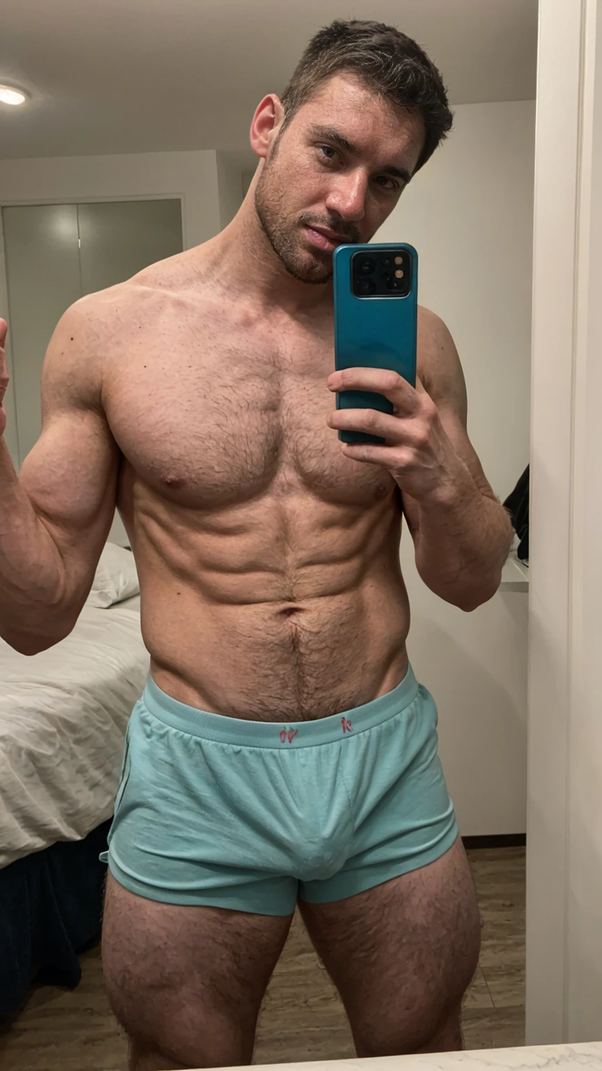 Real image of muscular and hairy man, short black hair, short beard, shirtless, wearing half turquoise and half white boxers. Taking a selfie with a black cell phone in a mirror.