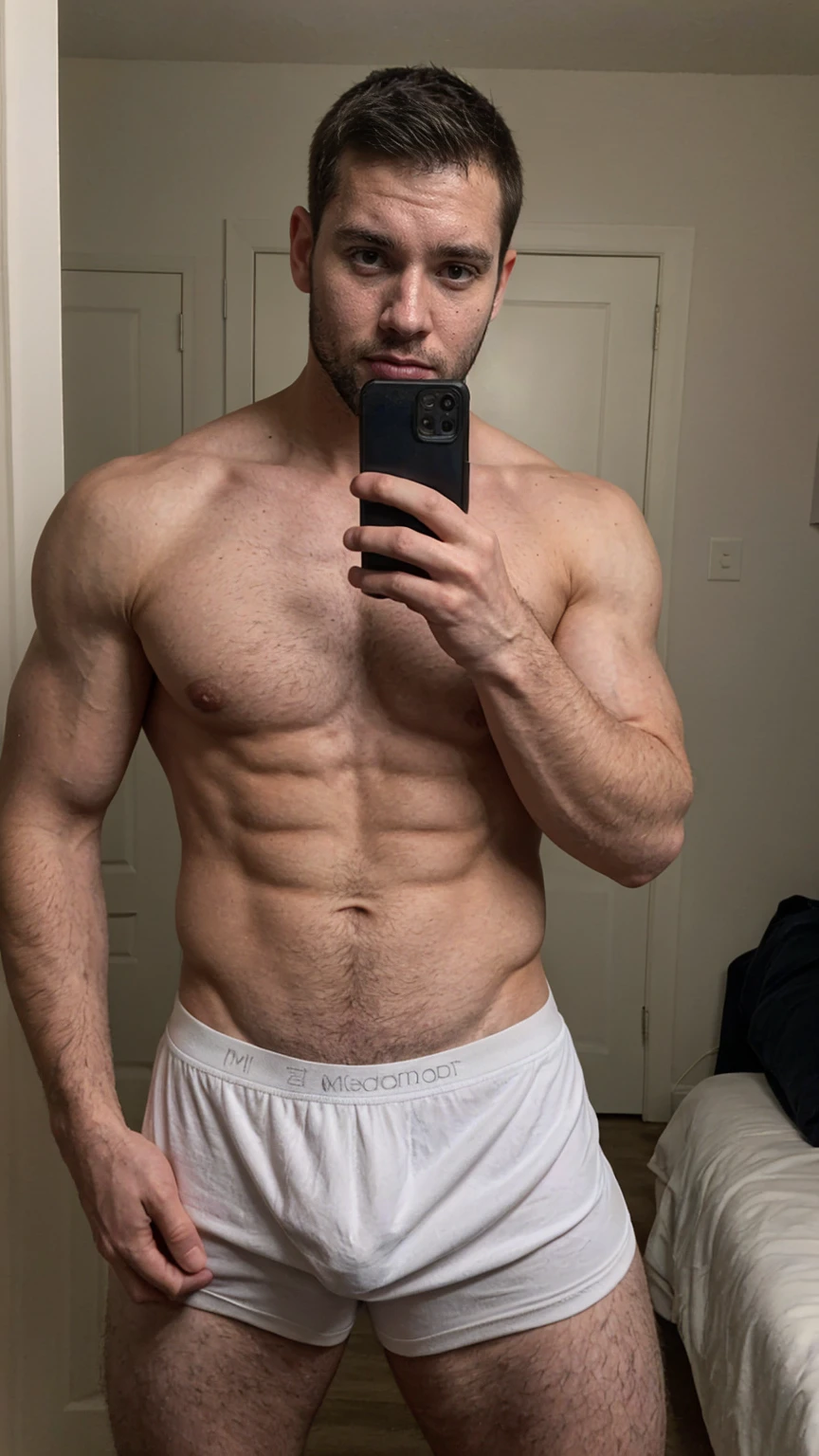 Real image of muscular and hairy man, short black hair, short beard, shirtless, wearing a white boxer. Taking a selfie with a black cell phone in a mirror.
