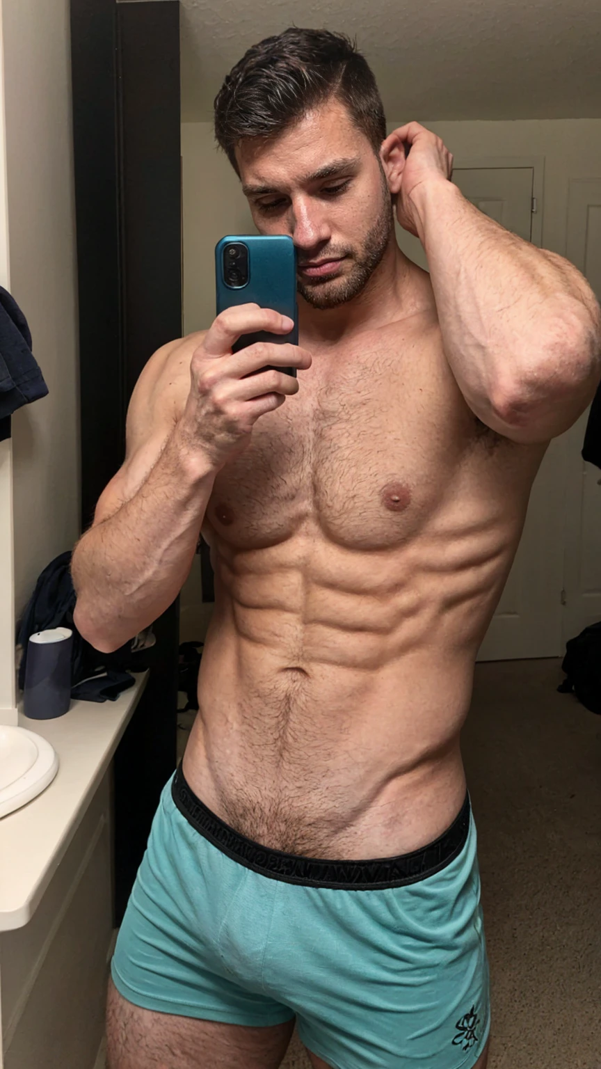 Real image of muscular and hairy man, short black hair, short beard, shirtless, wearing black boxers with turquoise patterns. Taking a selfie with a black cell phone in a mirror.