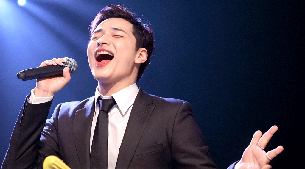 A man with his mouth wide open, shouting, eyes looking up, holding a microphone in his right hand