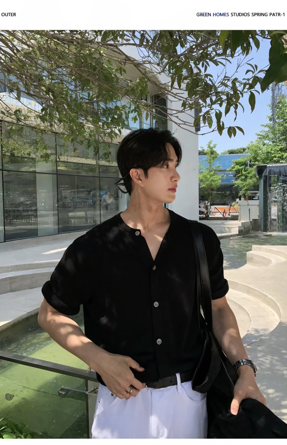 Portrait of a stylish young man with a cafe in the background。He was wearing a grey short-sleeved T-shirt and black pants.、It has a simple and modern style。His hair is neatly black.。His expression is serious、Facing to the side。A fashionable streetscape in the background。I feel class in the silver necklace.。He has a black jacket in his hands。The contrast of light and shadow makes his outline stand out.。
