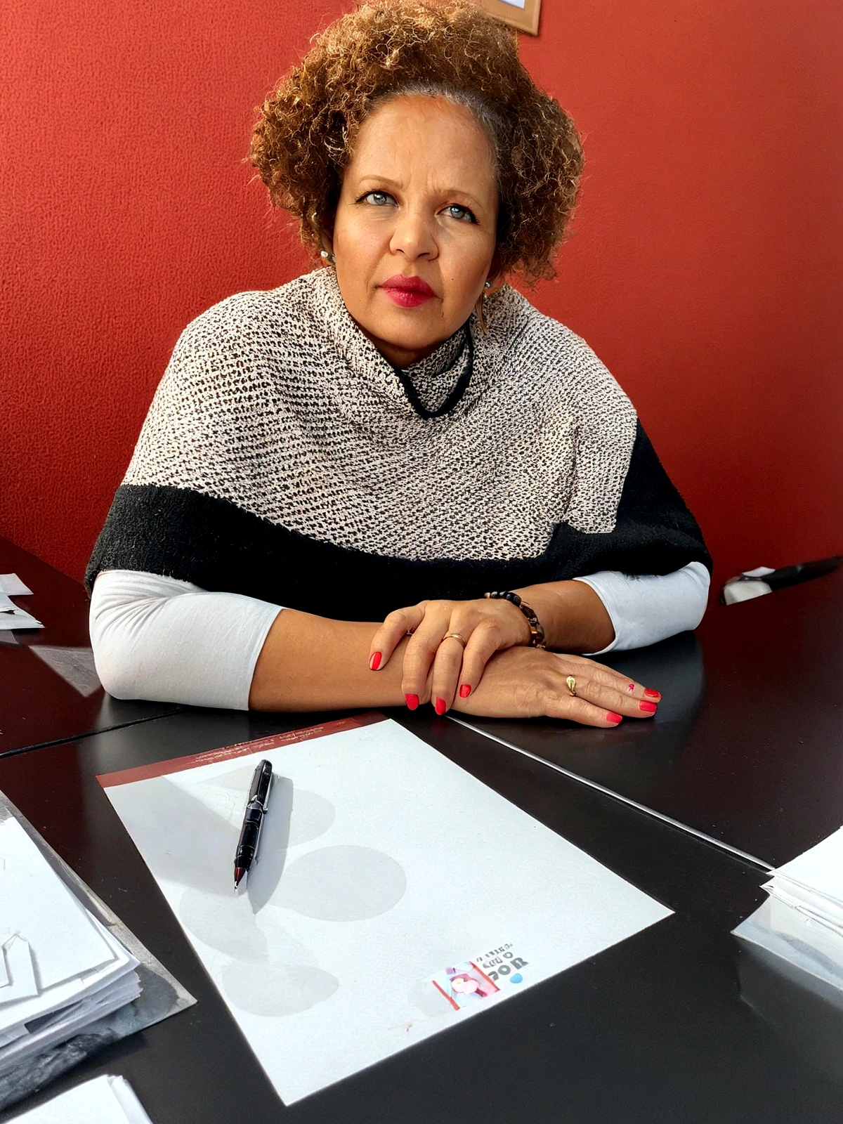 there is a woman sitting at a table with a pen and papers, photo of a black woman, on a desk, Portrait photo, taken at the beginning of 2020, photographic portrait, por Hubert van Ravesteyn, magnetic years, malika favre, Portrait photo, red afro, por Jesus Marie Lazkano, in the office