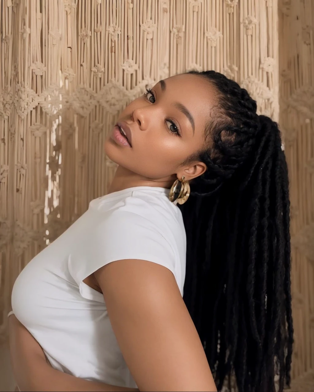 Black woman with braids with her body on her side looking at the camera with small eyes with the face diagonally.