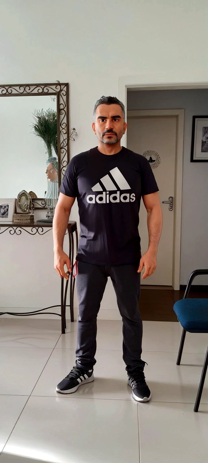 There is a man standing in a room with a mirror, wearing adidas clothes, photo by full body, ele está wearing a tshirt preta, wearing a tshirt e combate, wearing pants and t-shirt, wearing black tee, he is about 40 years old, he is about 40 years old, wearing a tshirt