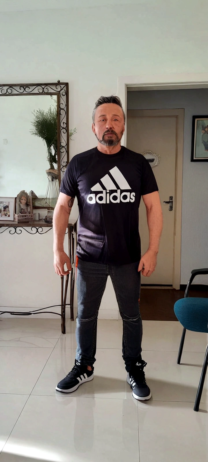 There is a man standing in a room with a mirror, wearing adidas clothes, photo by full body, ele está wearing a tshirt preta, wearing a tshirt e combate, wearing pants and t-shirt, wearing black tee, he is about 40 years old, he is about 40 years old, wearing a tshirt