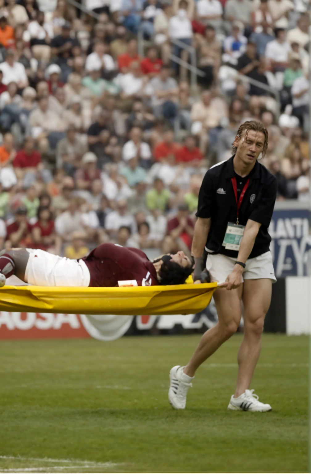 there is a male soccer player in short sportswear lying injured on a stretcher, there is an injured sportsman who is covering his face on a stretcher, an injured sportsman is covering his face with his hands, an injured sportsman is writhing ecstatic in pain on a stretcher, dramatic pity pose, there is a very female woman in a high-shine coat, a high-shine black wetlook coat, a long shiny coat, a wetlook glossy coat, a wet black laquered coat, a very female looking wife is wearing a wetlook coat, injured, medic, soccer action pose, affection pose, lecherous action pose, dramatic action pose, theatralic pose, there is an attractive woman that is carrying a suffering man on a stretcher, there is a beautiful woman in a shiny coat who is carrying a blond man on a wet orange stretcher, a longhaired beautiful woman in a high-shine coat, a longhaired woman in a shiny downcoat, a woman is carrying a stretcher with a shorthaired man who is wearing shorts and a t-shirt, a weak man in spots shorts is consciousless and needs to be carried on a wetlook pvc stretcher, a shorthaired man with closed eyes is carried on a stretcher by a longhaired woman, a woman looks very scared and terrified, a consciousless man with closed eyes is suffering very much and has a very painful face, photo, photo shoot, photographed , accident, help, aid, first aid, pity