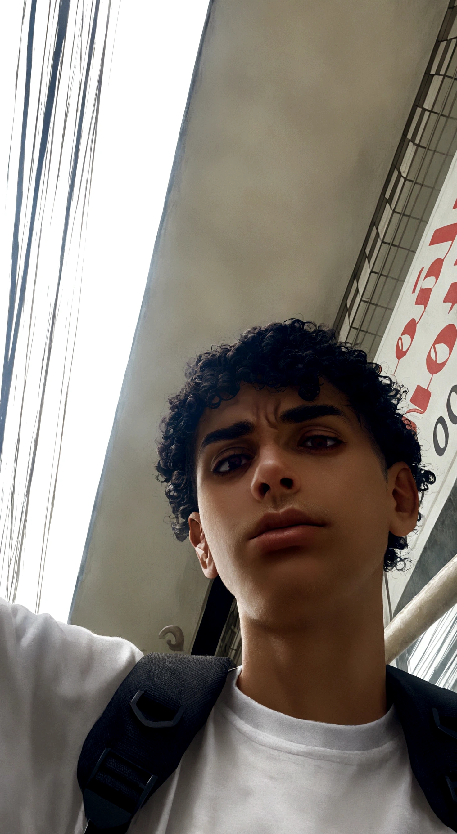 young man with dark curly hair, yellow mustache and serious face, with backpack on his back