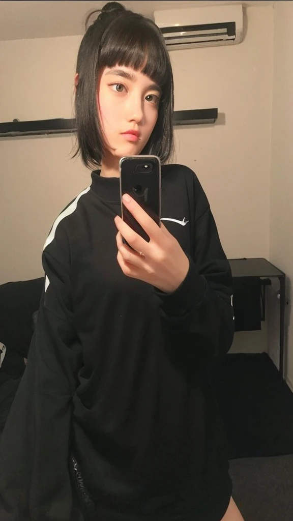 Pale teenage girl with black hair and bangs above her eyebrows, with small pink lips and a potato nose and light green eyes, taking a photo in the mirror with a black and white nike sweatshirt 