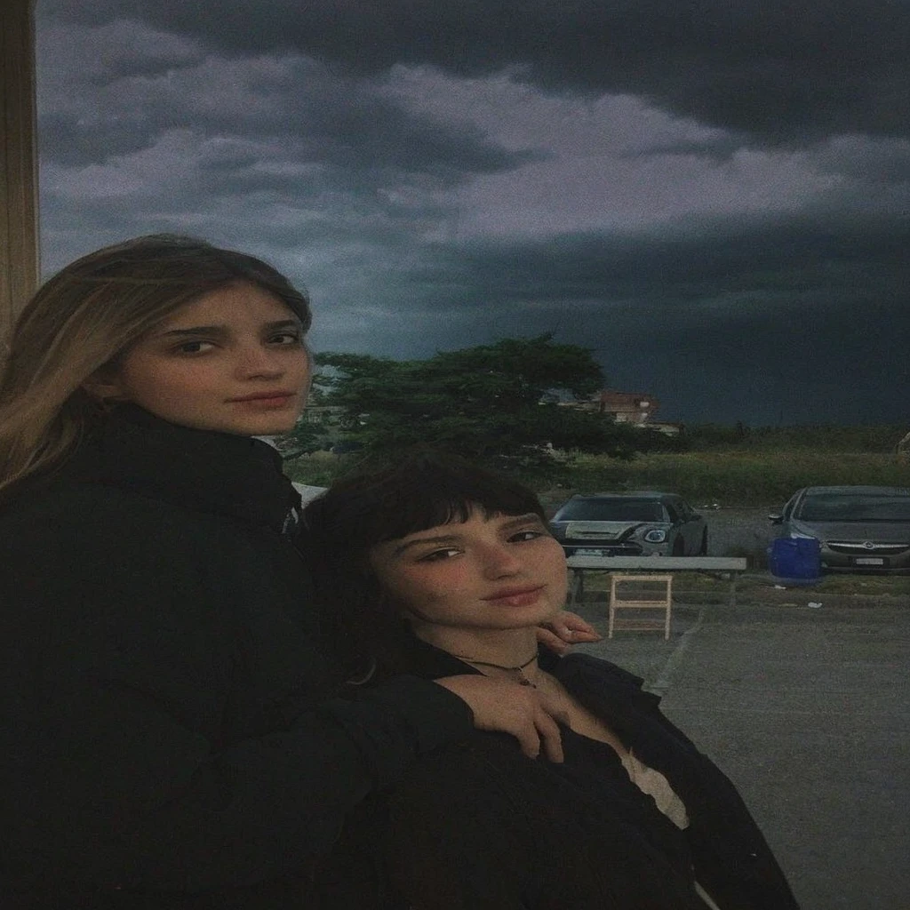 Pale teenage girl with silky black hair and bangs above her eyebrows, with small pink lips and a potato nose and light green eyes, taking a photo looking at the camera with your friend dark sky gray clouds and good quality
