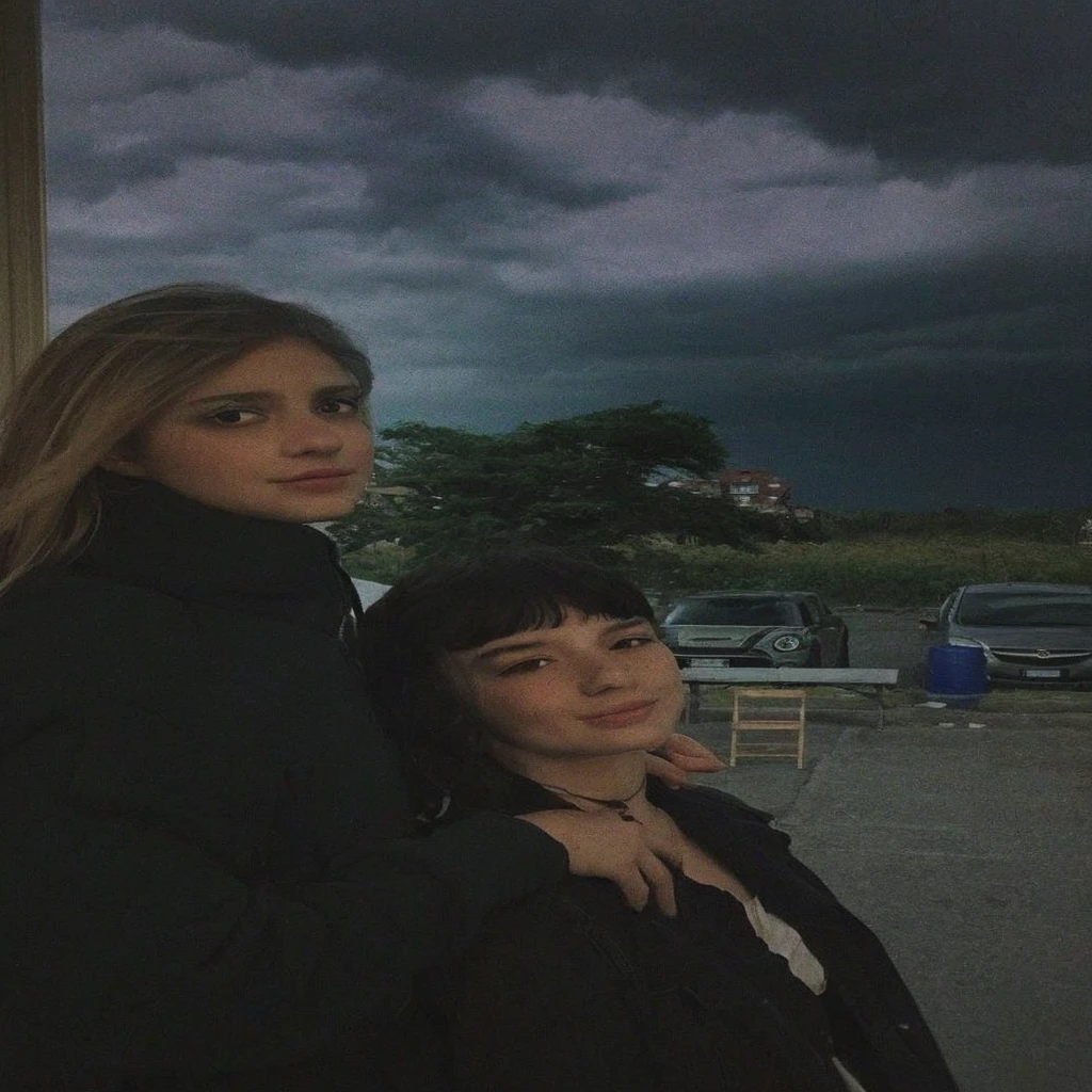 Pale teenage girl with silky black hair and bangs above her eyebrows, with small pink lips and a potato nose and light green eyes, taking a photo looking at the camera with your friend dark sky gray clouds and good quality 