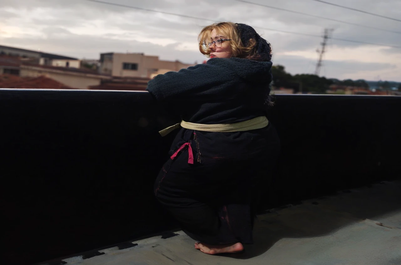 Slightly chubby blonde woman, of square glasses, blondie hair, clear green eyes, on the balcony looking at the sea to the horizon at sunset