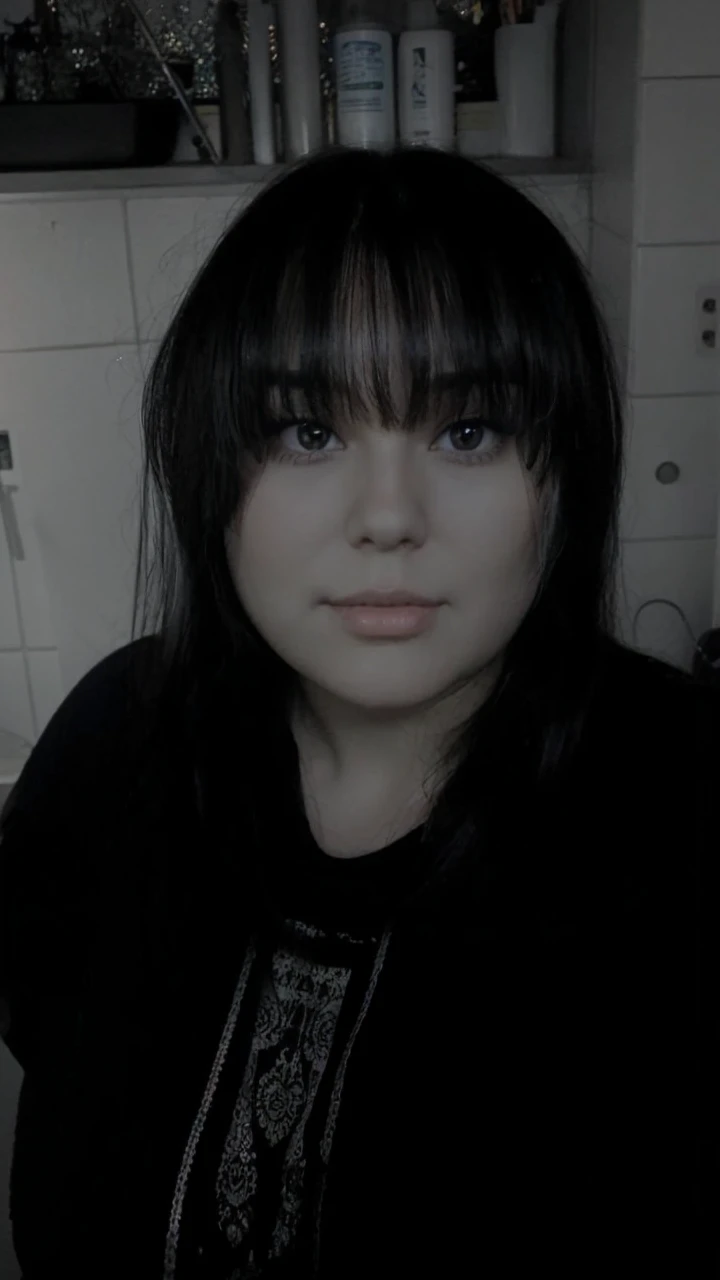 A super pretty woman with long black hair with some bangs. She has some cheeks and brown eyes. She weighs about 86 kg. She is a bit chubby. She comes from Germany