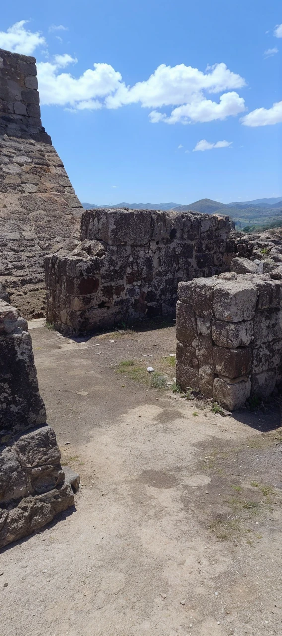 18-year-old girl similar to Chloë grace Moretz, smiling, waist-length red hair, disheveled and disheveled, wearing a white fedora hat, white sleeveless blouse, blue miniskirt, tennis shoes, no socks, tight clothing, posing on a frame of ruined stone, probably part of an ancient construction, completely exposed to the sun. The stones are arranged so that they form walls of different heights. In the background you can see a mountainous landscape under a clear sky with some clouds. As for the type of lighting, the photo appears to be taken during the day in direct sunlight. This can be inferred from the defined shadows and bright light illuminating the stones and ground, as well as the clear blue sky. super realistic, perfect body, correct proportions and perspectives, masterpiece, photo realistic, natural lighting from direct sunlight, outdoors