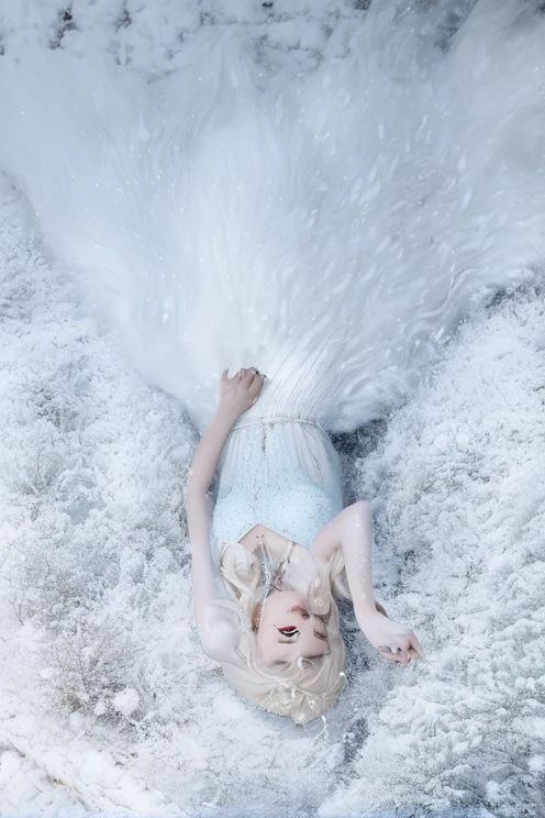 A girl with white hair in a blue dress lies in the snow