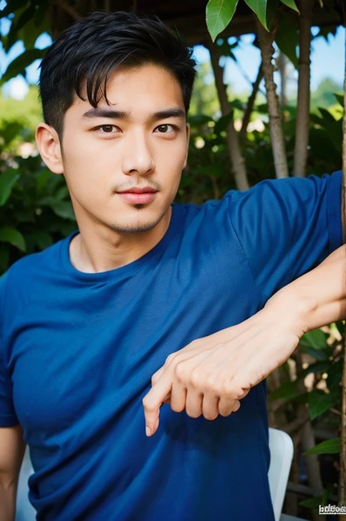 A handsome, muscular young Asian man looks at the camera. In a simple blue t-shirt , Fieldside, grass, beach, sunlight