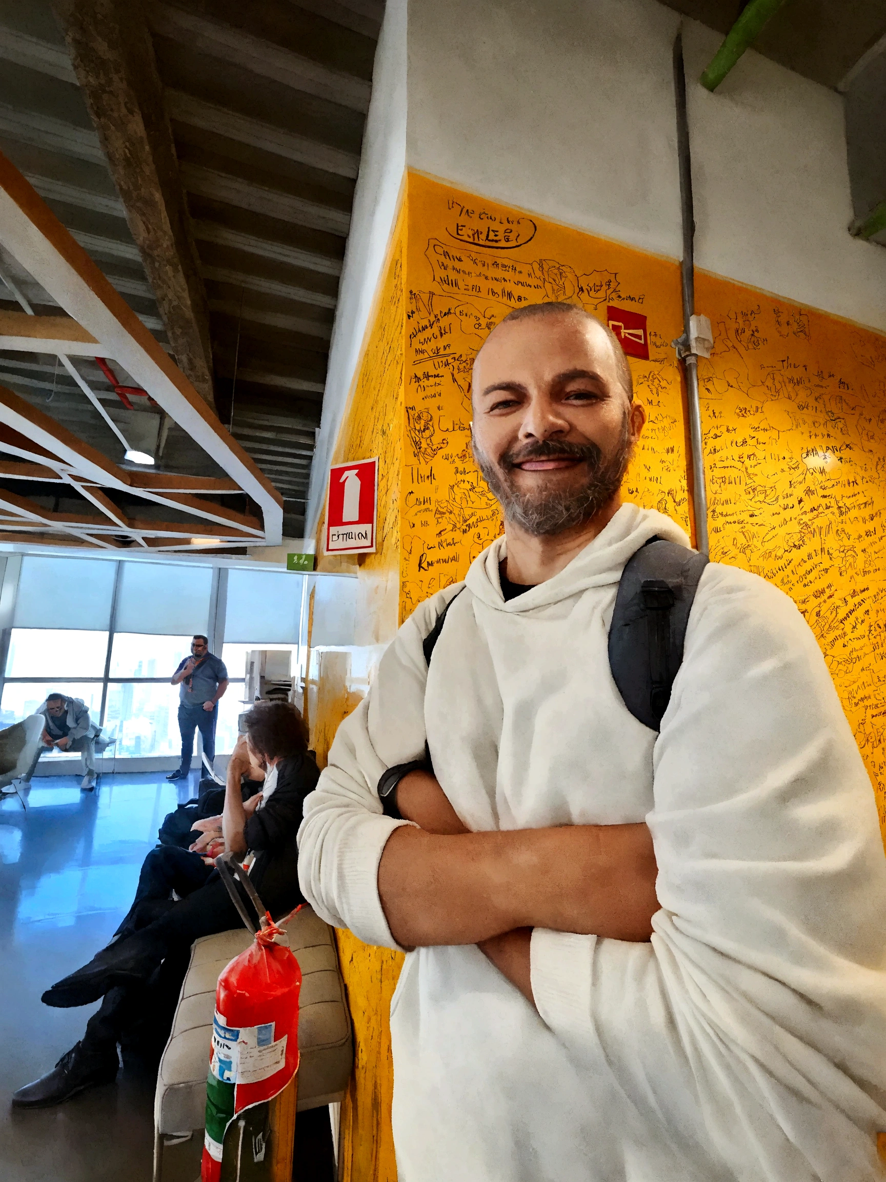1.86 meter man. With a sparse beard and shaved hair. Man of Brazilian origin smiling in an office and wearing a white hooded sweatshirt