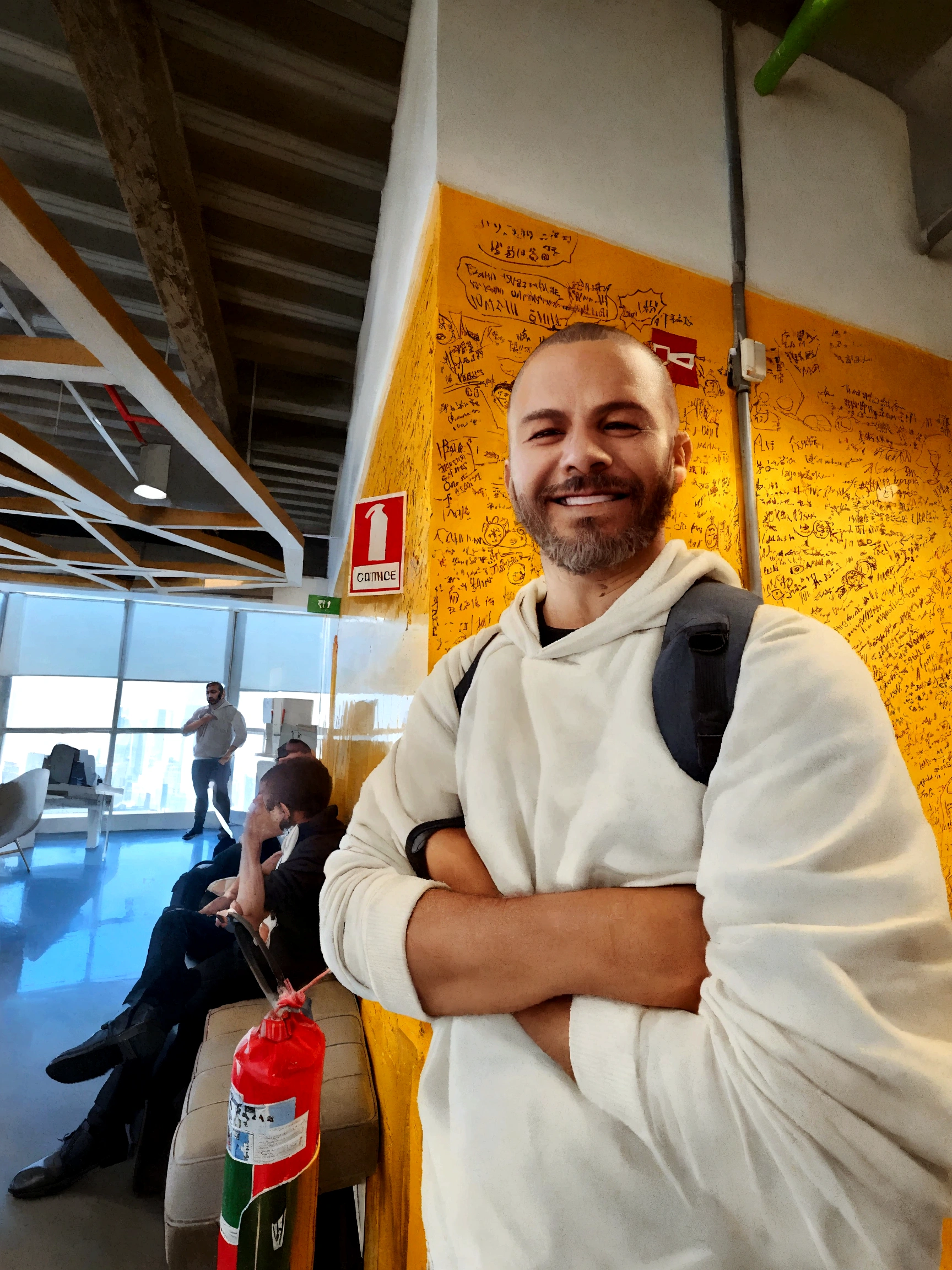 1.86 meter man. With a sparse beard and shaved hair. Man of Brazilian origin smiling in an office and wearing a white hooded sweatshirt
