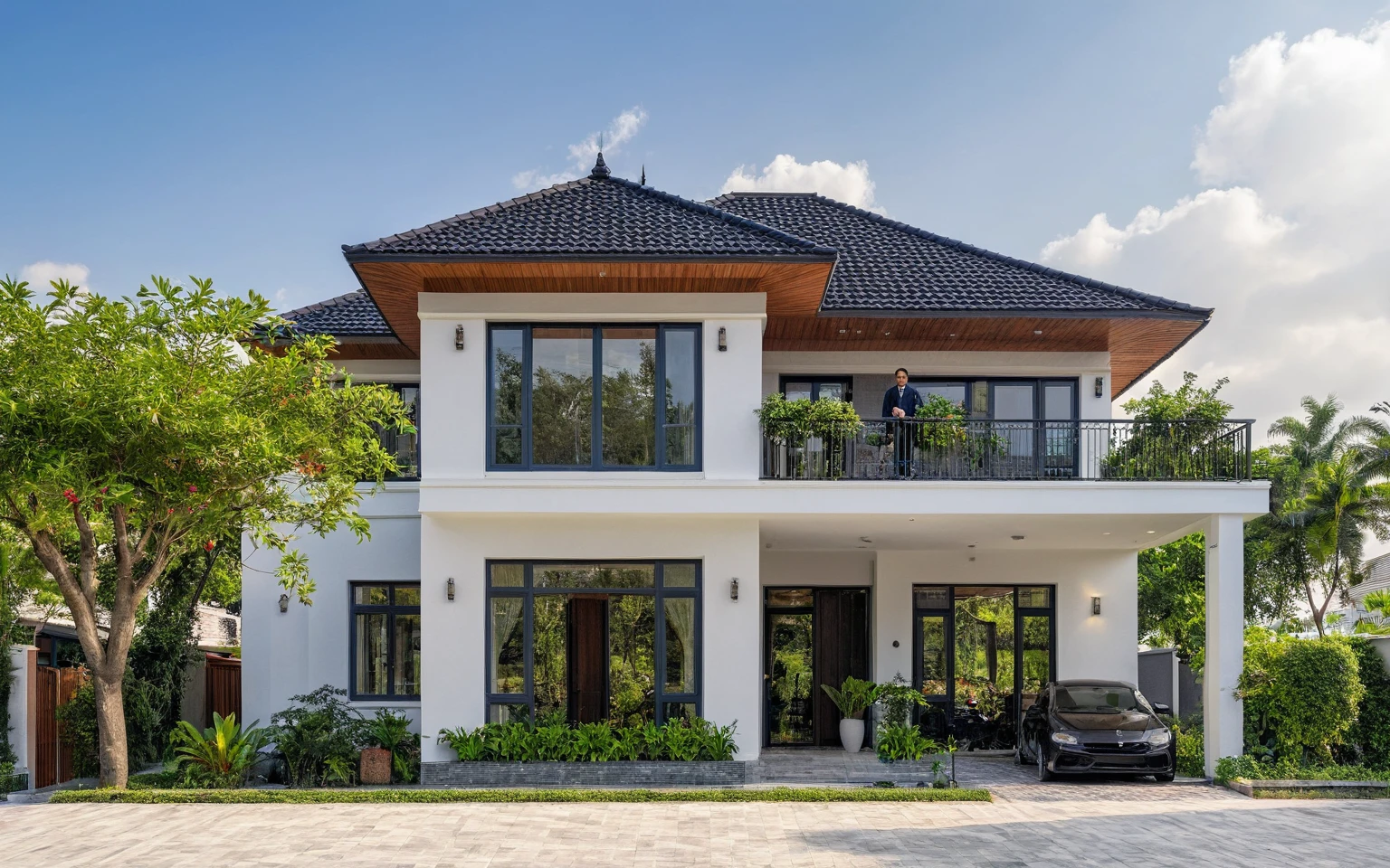 (masterpiece:1.2), best quality, photo of A two-story modern house in VietNam with white walls and dark tiles on the roof., wooden wall is accent, tree and plant environment,daylight, streetcapes, natural light, vivid color, The exterior of an elegant single family home features large windows, a dark gray door frame.