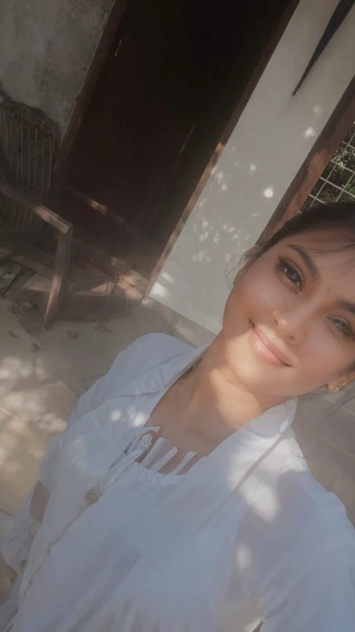 A charming indian woman, with an Off-the-shoulder shirt, Pelvic Curtain, necklace, Portraiture, bracelet, Cowboy Shot, Seductive pose, smile. Her soft dimples and realistic expression lines add authenticity. Her skin is illuminated by the sun's rays, highlighting her beauty. She is dressed in long, sophisticated clothes. In the background, there is a chaotic structure with multiple entrances, almost in ruins, surrounded by dense and branched vegetation. To capture this extraordinary scene, a high-resolution camera such as the Phase One XF IQ4 150MP is required. The lighting is diffused and natural, minimizing harsh shadows. The camera settings include a medium aperture, adjusted shutter speed, and a high-quality wide-angle lens with a focal length of approximately 35mm to capture the entire scene in an immersive way. Sharp, precise details are captured, from wavy hair to complex clothing patterns, ensuring a natural and stunning image.