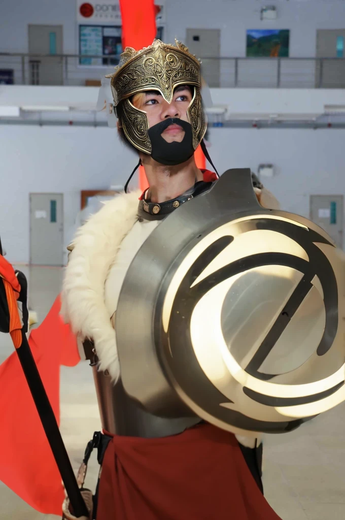 King Leonidas wears a classic Spartan helmet, also known as a Corinthian helmet. It has a bronze finish with a high crest of red and black horsehair, signifying his rank as a king. The helmet covers the entire face except for the eyes, nose, and mouth, providing maximum protection while allowing him to see and breathe easily. The edges are decorated with intricate patterns and engravings.
Armor: His armor is made of bronze and consists of a cuirass (breastplate) with muscle sculpting to emphasize his physical prowess. The cuirass is ornately decorated with engravings of mythical creatures and battle scenes. He wears a red cloak draped over his shoulders, secured with a golden brooch. His greaves (shin guards) and bracers (forearm guards) are also made of bronze and bear similar decorative patterns.
Face: Leonidas has a rugged, determined expression, with a well-defined jawline and a thick beard. His eyes are intense, reflecting his warrior spirit and unwavering determination. His face shows the marks of past battles, with a few scars that add to his fierce appearance.
Spear: He holds a long Dory spear, which is the primary weapon of a Spartan hoplite. The spear is approximately 8 feet long, with a wooden shaft and a leaf-shaped iron spearhead. The shaft is reinforced with metal bands for extra durability, and the butt end is fitted with a bronze counterweight called a sauroter, which can also be used as a secondary weapon.
Shield: Although not specifically requested, it’s worth noting that Leonidas carries a large round shield known as an Aspis or Hoplon. The shield is made of wood, covered with bronze, and emblazoned with the symbol of Sparta, a lambda (Λ).