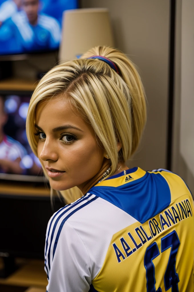 A blonde woman wearing a Colombian soccer jersey with the name Alejandra on the back watching the game on the television