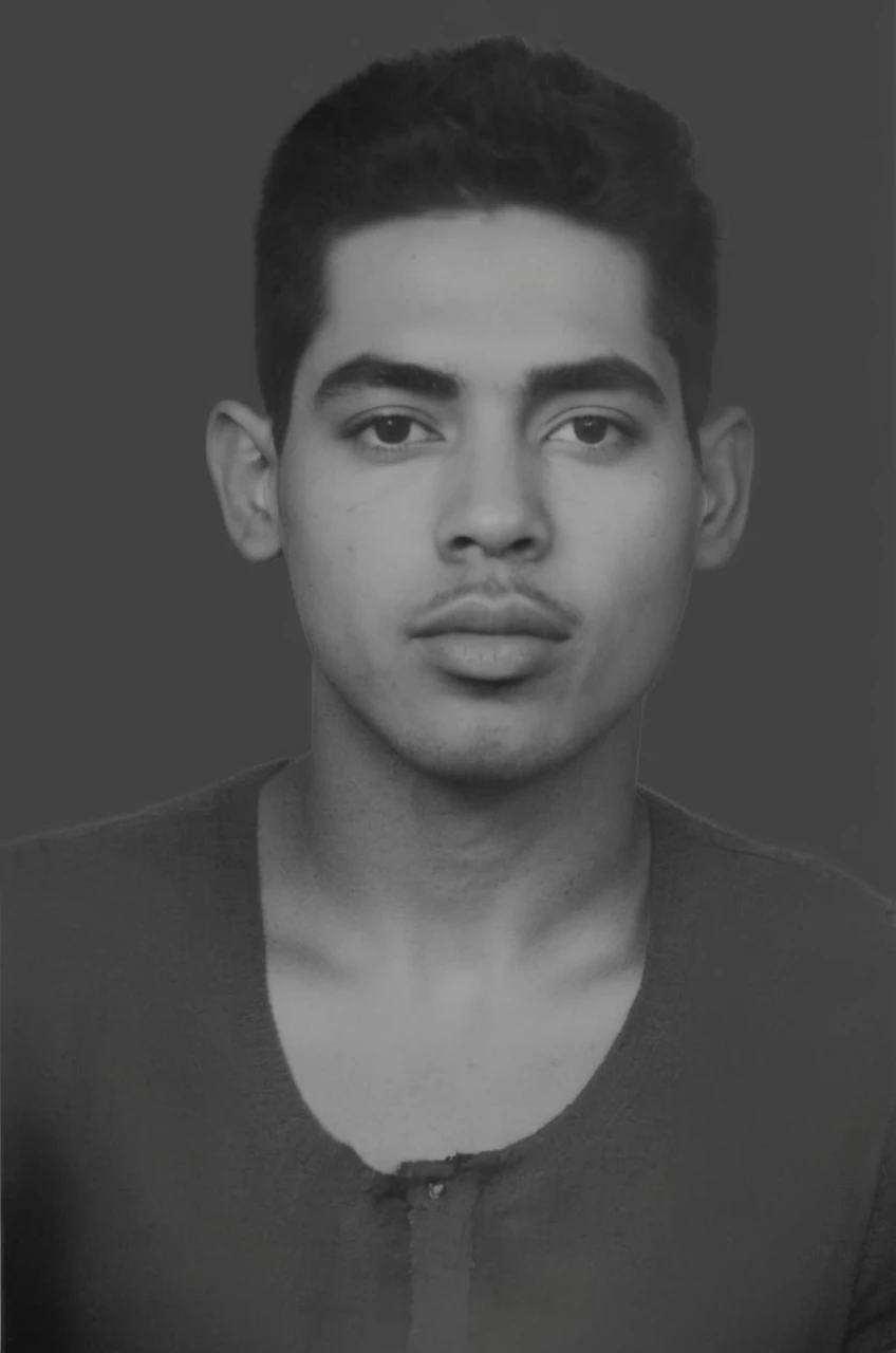 Portrait of a young man with a neutral expression, short dark hair with a faded cut, bushy eyebrows, and full lips. The person has a medium skin tone and is wearing a dark, round-necked shirt. The background is a solid, flat color.