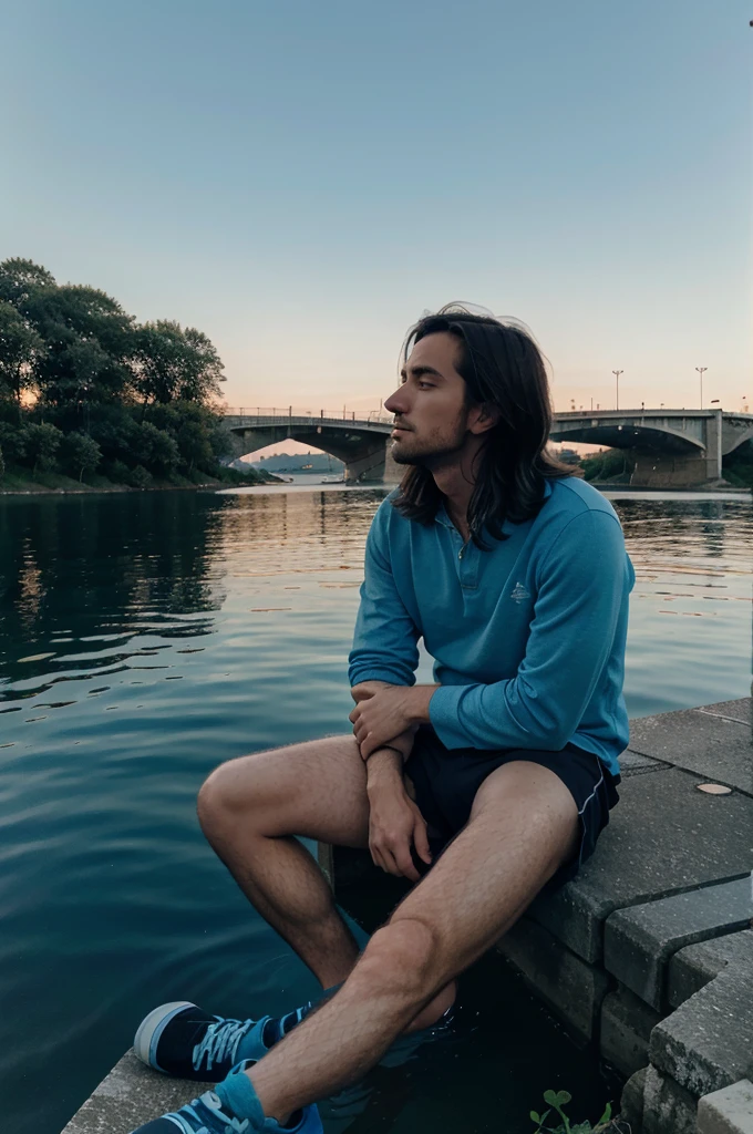 A man under the blue sky sits on the edge of the lake at the edge of the bridge at dusk