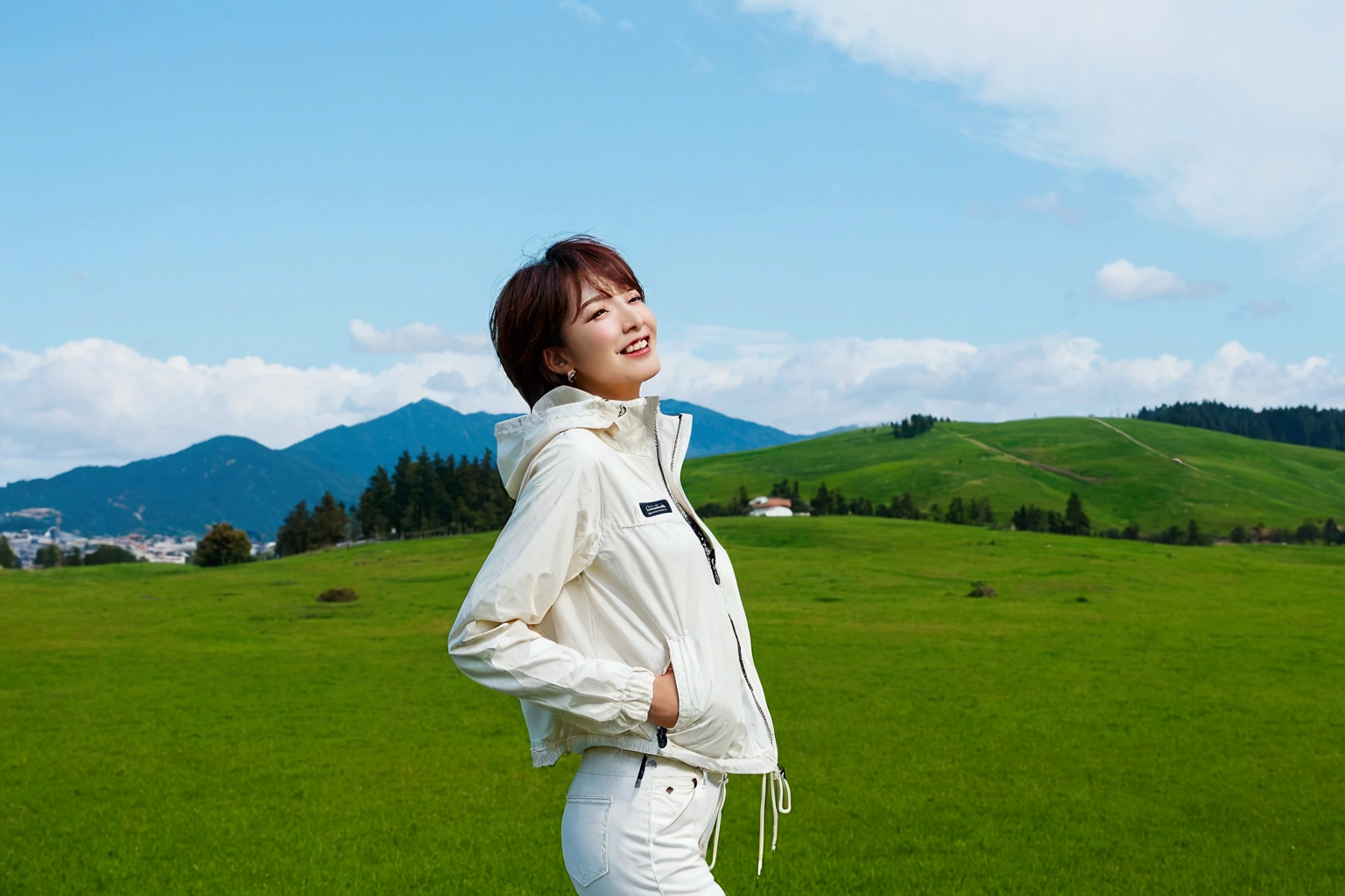 high quality, 1 woman, ((36 years old 건강한 한국 여성)), ((36 years old)), 1 woman, The eyes are big and beautiful. ((slim)), ((short medium hair)), laugh. pose: standing, High-end luxury brand windbreaker jacket, white casual pants, background: 1 woman, California, pasture, Cow, grass. Full body shot with 16-34 wide angle lens, look up to the side, blue sky, So that you can see the whole body